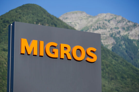Migros orange company logo sign with alpine mountains background in Contone
