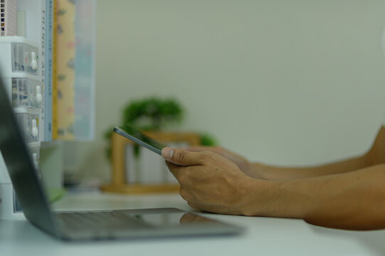 Person Using Smartphone at Desk with Laptop and Office Supplies in Background