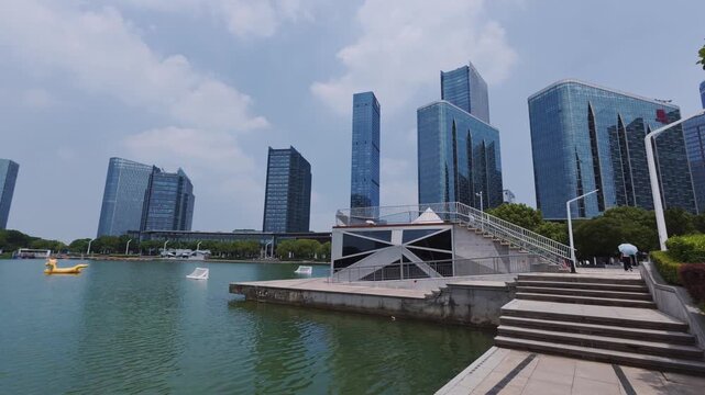 A modern urban skyline with glass skyscrapers lining a calm waterfront under a partly cloudy sky.