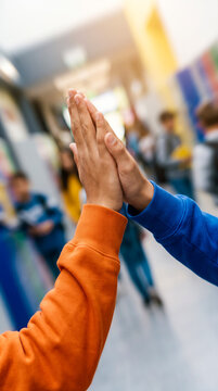 Two students giving high five in school hallway. Education, teamwork, friendship, student life, positive interaction.