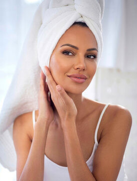 Beautiful woman with towel wrapped around head gently touching her face after bath.