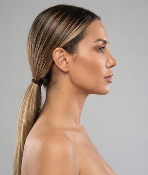 Side profile view of a beautiful woman with a sleek ponytail posing against grey background.