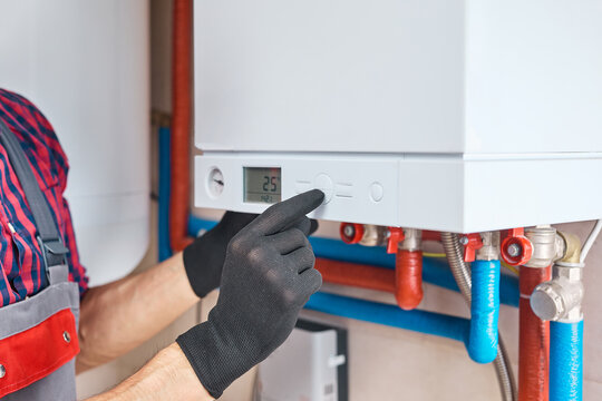 Plumber adjusting the temperature on a central heating boiler's control panel, ensuring optimal performance and energy efficiency in a home