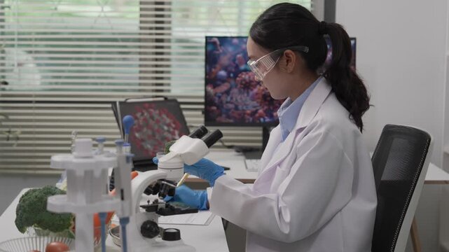 An Asian female food scientist wearing safety glasses and gloves holds fresh broccoli and carrots, inspecting their quality for pesticide residues or chemical contaminants in a food research laborator
