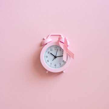Breast cancer awareness month pink alarm clock with ribbon on soft square pink background reminding time for screening and support
