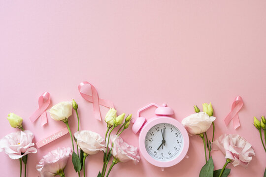 Breast Cancer Awareness month concept with pink ribbon, alarm clock and flowers on soft pink background