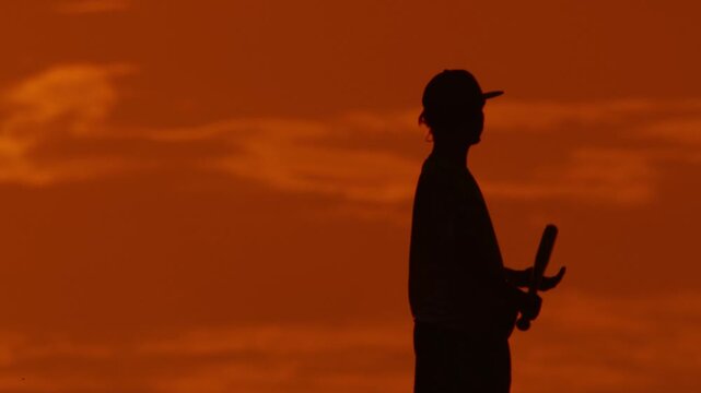 Baseball player stands with bat during sunset at the field
