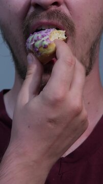 Man takes a bite from a pink donut held in his hand in a kitchen setting