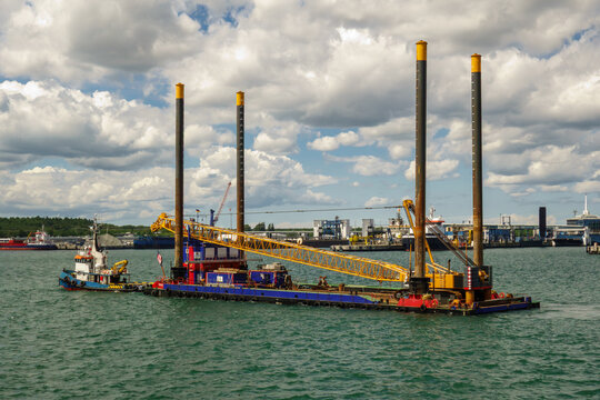 Industrial Jack-Up Barge with Crane Towed by Tugboat in a Port. Marine Construction and Offshore Engineering Platform in Harbor.