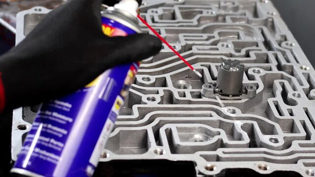 Close up of a mechanic applying lubricant spray from a can to clean the intricate fluid channels.