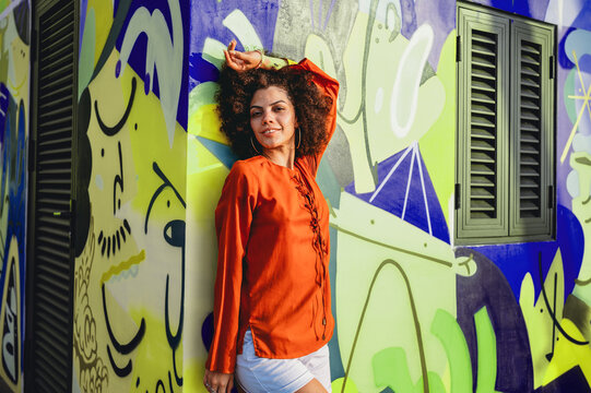 Beautiful young woman smiles warmly in a vibrant portrait against colorful street art on a sunny day