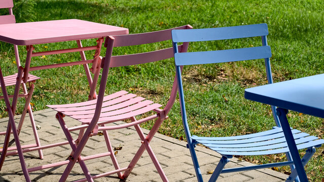 Outdoor cafe furniture in pastel pink and blue, creating a vibrant, inviting atmosphere on a paved patio with green lawn, perfect for relaxing summer days and social gatherings