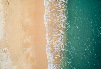 Fototapeta premium Aerial view of sandy beach and turquoise ocean. Top view of ocean waves reaching shore on sunny day.