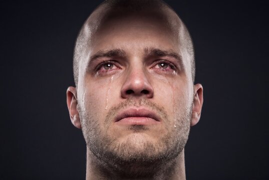 Depressed young man crying with tears on face in emotional portrait