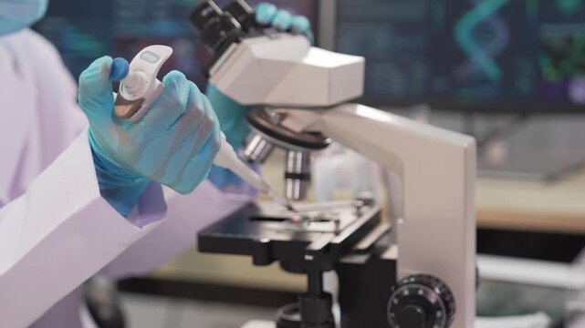 A close-up shot of a female scientist wearing blue gloves pouring various colored liquid chemicals from a bottle into a glass beaker inside a medical or chemical laboratory&mdash;a research concept.