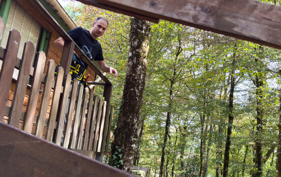man on an extension ladder using a hammer to nail in new wood siding boards, homeowner maintenance and upkeep, making outdoor repairs on house 