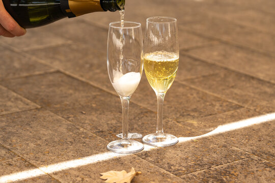 Close-up of sparkling champagne being poured into two elegant glasses on a stone terrace. Golden bubbles, bright sunlight, and a refreshing summer vacation mood.