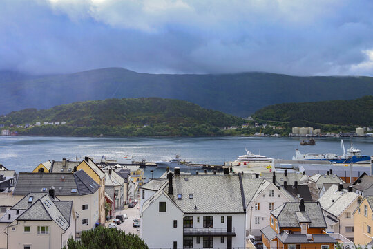 Traditional coastal houses and harbor in Alesund town, Norway. Scandinavian cityscape with ocean bay, mountains under dramatic sky.
