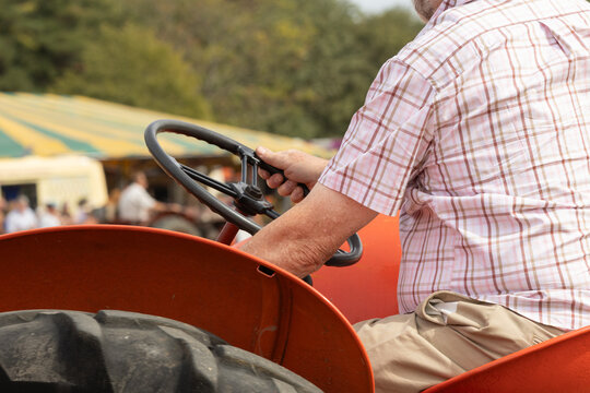 Close-up of a man sat driving a vintage red tractor at a country show. 