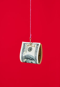 One hundred dollar bill on fishing hook over red background