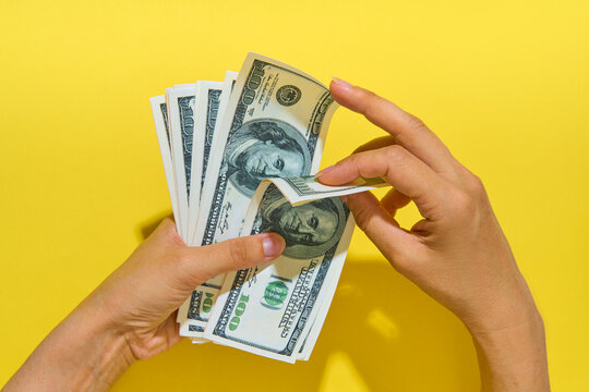 Hands counting hundred dollar bills on yellow background