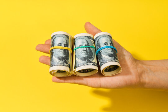 Hand holding three rolls of hundred dollar bills