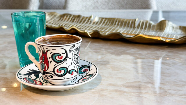 Traditional Turkish coffee in a colorful ceramic cup with a glass of water on a marble table, cozy coffee break and cultural beverage concept.
