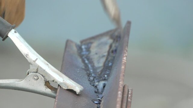 Industrial welder cleaning a joint with a chipping hammer in a fabrication shop. Extreme close-up static shot.