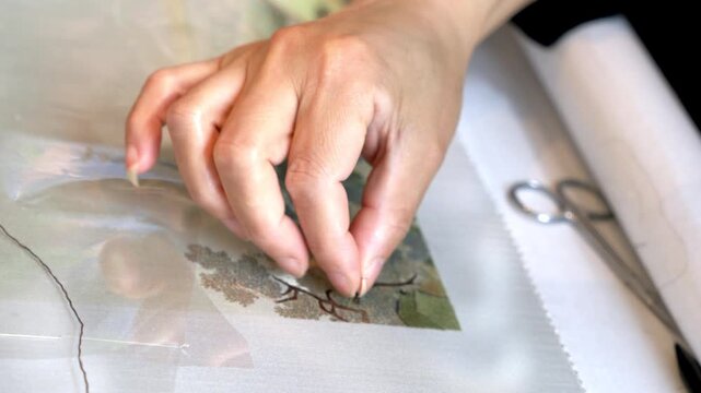 A person's hand works on a craft project with scissors and patterned printed material on a workspace.