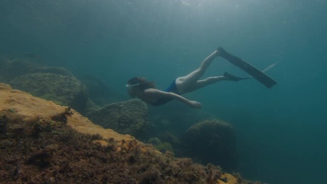 Young slim woman swims underwater, freediving and snorkeling in the sea near the coral reef near the island of Ilha Grande in Brazil