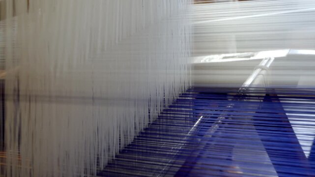 A weaving loom holds white and blue threads, used for textile production in a workshop setting.