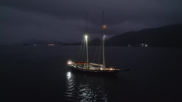Big expeditional sailing boat anchored in the calm sea at night. Drone night shot