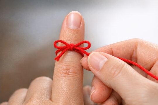 A person wraps a red string around their finger, possibly indicating good luck or protection