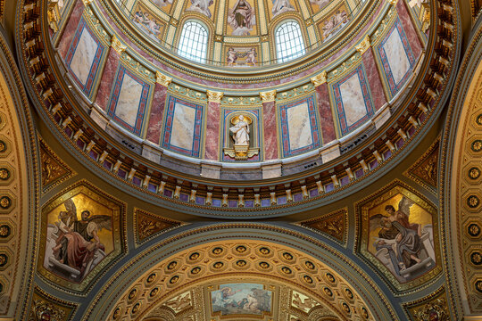 Tiered coffered dome with mosaic saint portraits and arched windows inside Saint Stephen's Basilica in Budapest