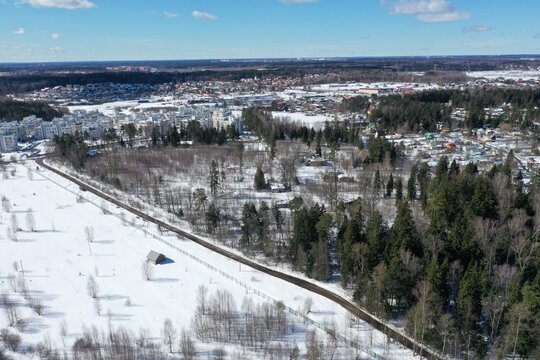 Aerial winter view of a snowy forest with cottages and a distant town