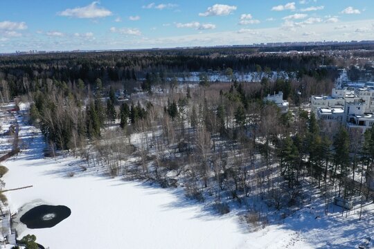 Aerial winter view of a snowy forest with cottages and a distant town