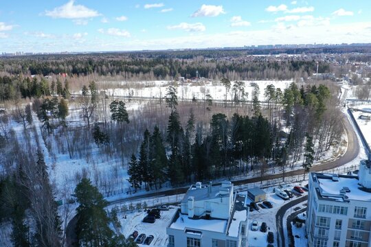 Aerial winter view of a snowy forest with cottages and a distant town