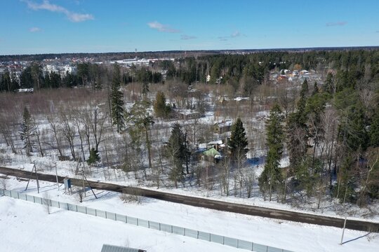 Aerial winter view of a snowy forest with cottages and a distant town