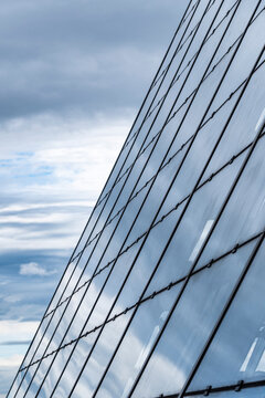 A diagonal view of a modern building turns glass facade and reflection into a minimal study, with architecture set against sky and layered clouds