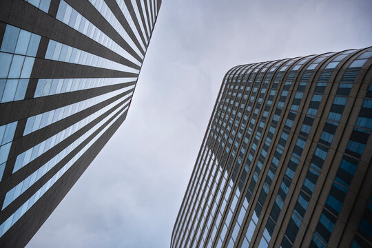 Two towers shape a modern architecture scene in upward view, where glass facade, urban lines and a subtle curve open toward a pale sky