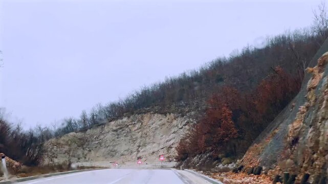 Driving on a rainy mountain serpentine road through windshield with wipers. View from inside a car driving along a winding mountain serpentine road in rainy weather. 