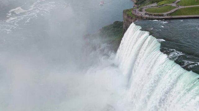 Aerial view circling left over the powerful crest of the American Falls, moving directly into the heavy white mist and spray rising from the basin below