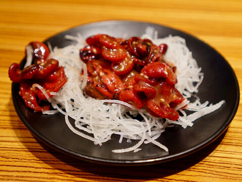 Close-up shot of Japanese chuka idako seasoned baby octopus served on a bed of shredded daikon radish in a black plate