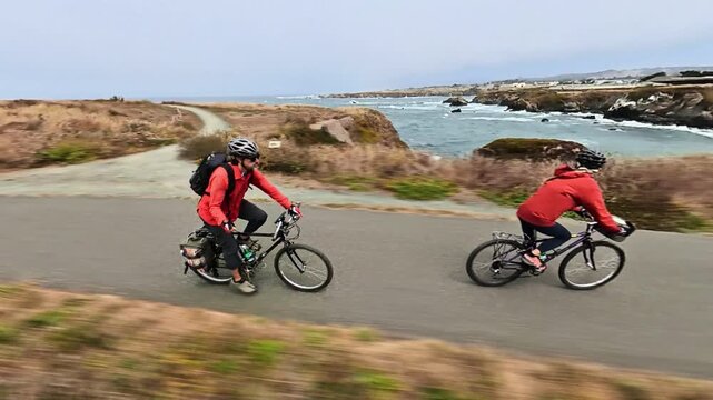 A couple rides bicycles along the Noyo Coastal Trail with views of cliffs, ocean, and beach in Fort Bragg California.