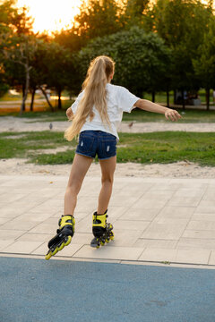 A lovely fair-haired girl is skating on yellow roller skates in the golden hour sunlight