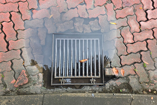 Overhead view on puddle of water on clogged drain outlet with leaf on street risk flooding during heavy rain