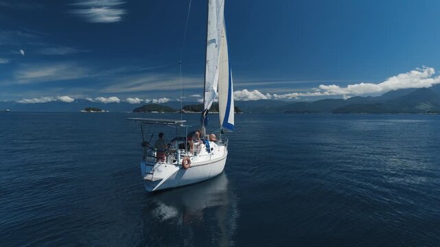 Sailing boat moves in the tropical sea near the Brazilian shore during nice sunny day. Couple sailing the small sailing yacht in the sea. Aerial drone shot of the sailing boat