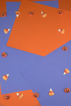 Halloween background featuring scattered pumpkin candies and candy corn on orange and purple paper, creating a festive border