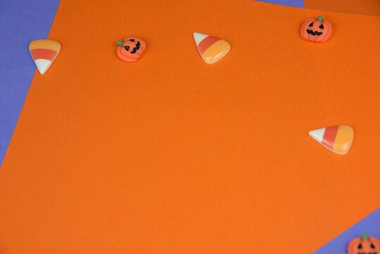 Halloween candy corn and small pumpkins on a vibrant orange and purple background, creating a festive fall border