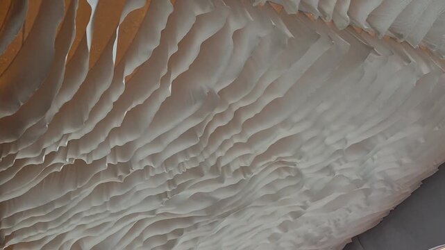 Decorative white fabric drapery gently moving and rippling in the air, creating a dynamic suspended textile ceiling with a soft flowing texture. Abstract architectural background with neutral tones an